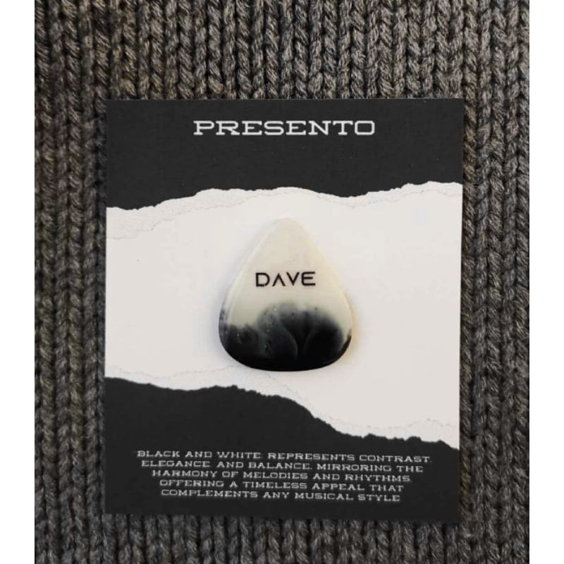 A Customized Guitar Pick featuring the name "DAVE" is displayed on a card that discusses how black and white symbolize contrast, elegance, and balance. It rests on a knitted surface.