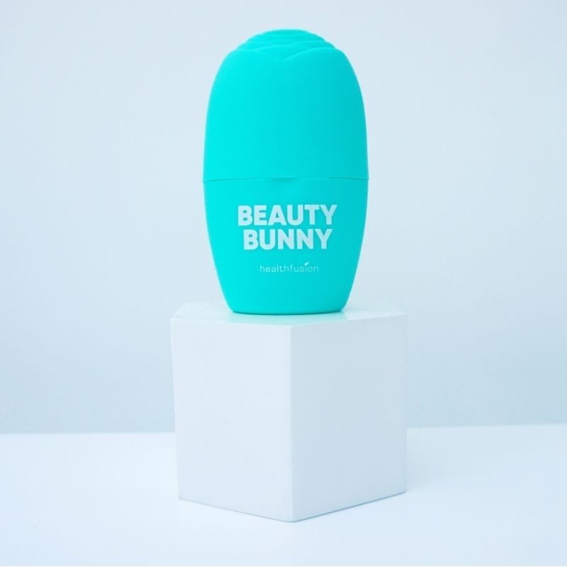 A teal "Beauty Bunny" product container from Healthfusion, paired with the ELAIMEI Egg-shaped Ice Mold Ice Face Roller, positioned on a white cube against a light background.