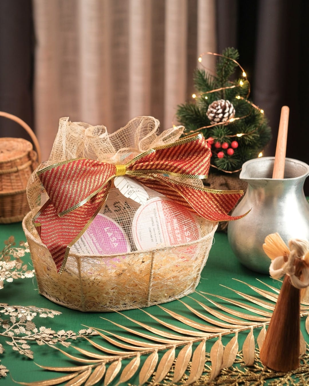 A basket with a LASA Tsokolate Gift Sets and a christmas tree on a green table.