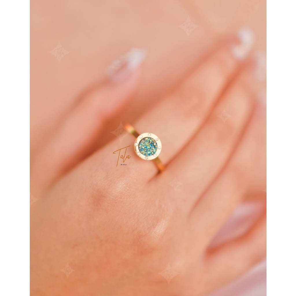 A woman's hand holding a Tala by Kyla My Universe Fidget Ring with a blue topaz stone.