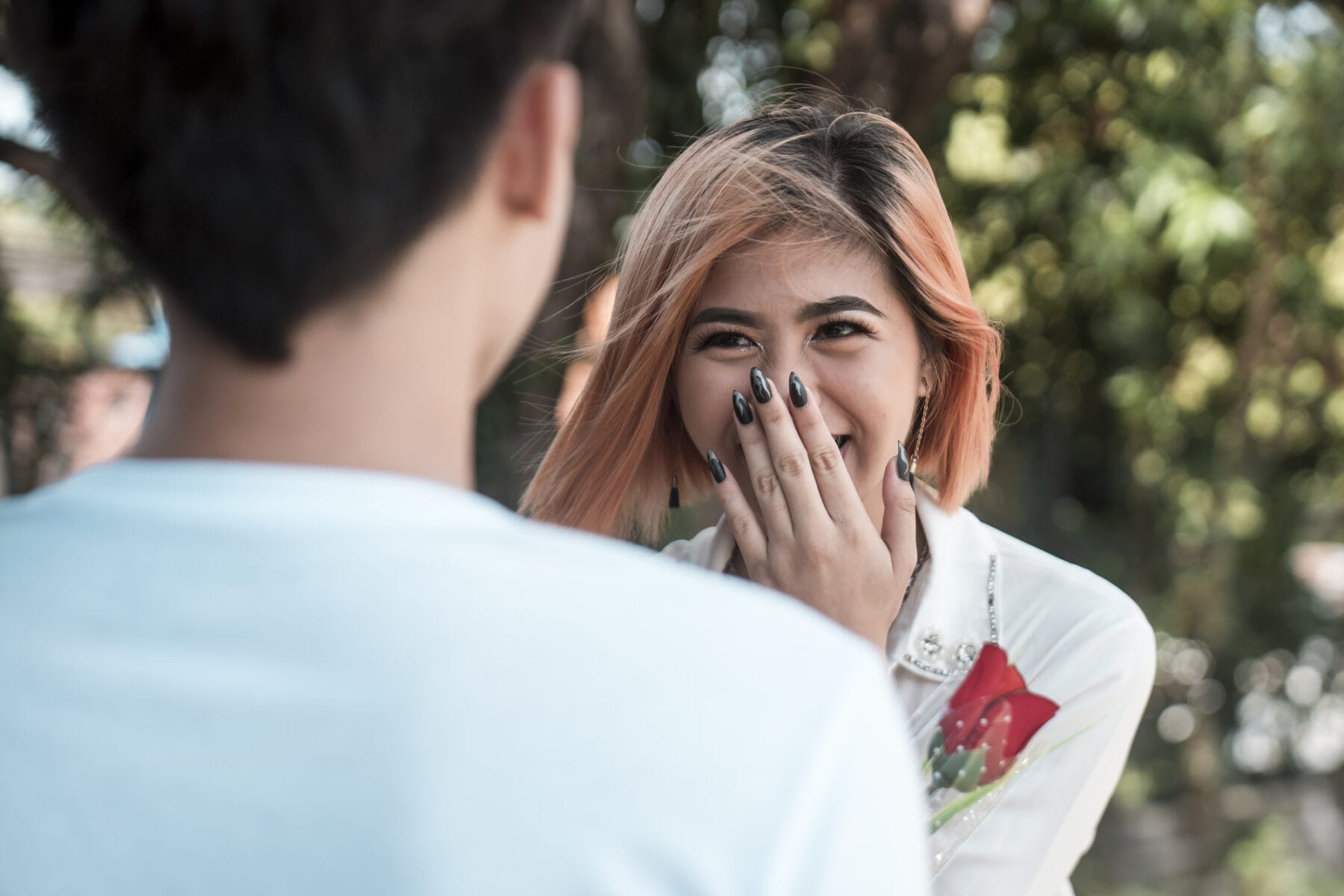 Woman with orange hair smiling and covering her mouth with her hand, facing a man in a white t-shirt who represents the mu of their relationship, blurred in the foreground. My meaning in relationships
