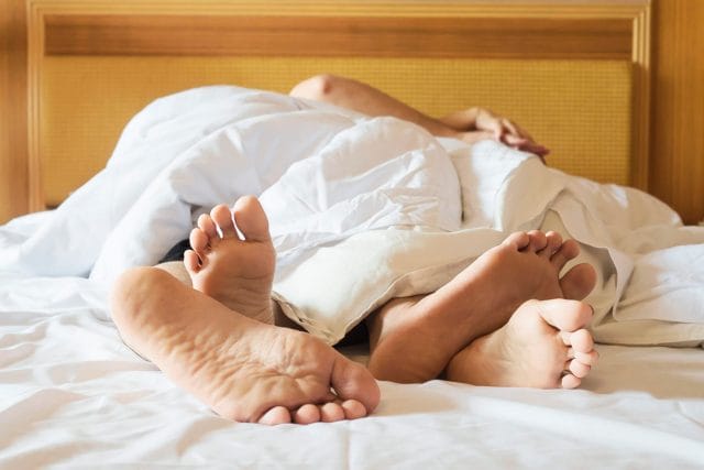 A couple lying in bed, only their feet visible above the white sheets, suggesting a relaxed or intimate moment. honeymoon tea